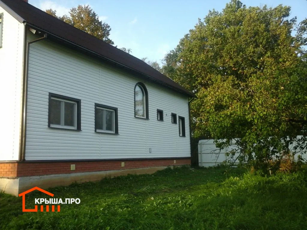 Отделка фасада сайдингом Döcke в селе Раменье: 225 м² за полторы недели — объект №17 - Фото 8 Фасад дома с арочным окном, обшитый сайдингом, проёмы обрамлены тёмно-коричневыми планками