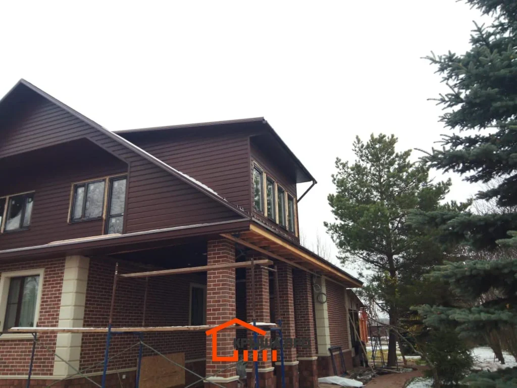 Замена кровли с утеплением в деревне Потапово: гибкая черепица Katepal, 283 м² — объект №75 - Фото 19 Дом с новой кровлей и обшитыми фронтонами, у стены ещё стоят леса