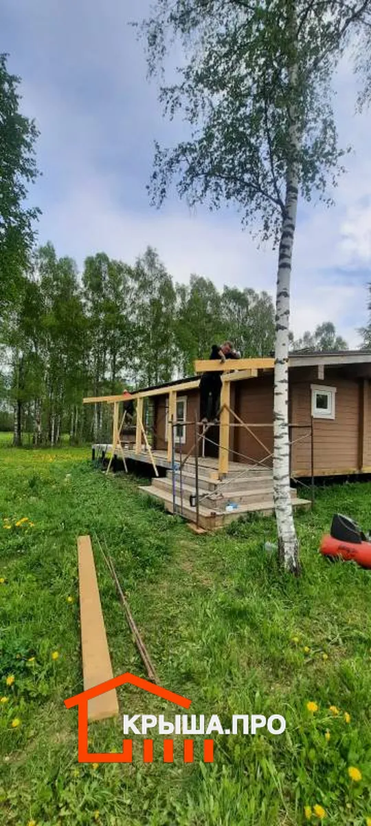 Начало монтажа навеса: стойки из бруса установлены на террасе, монтажник у примыкания к дому